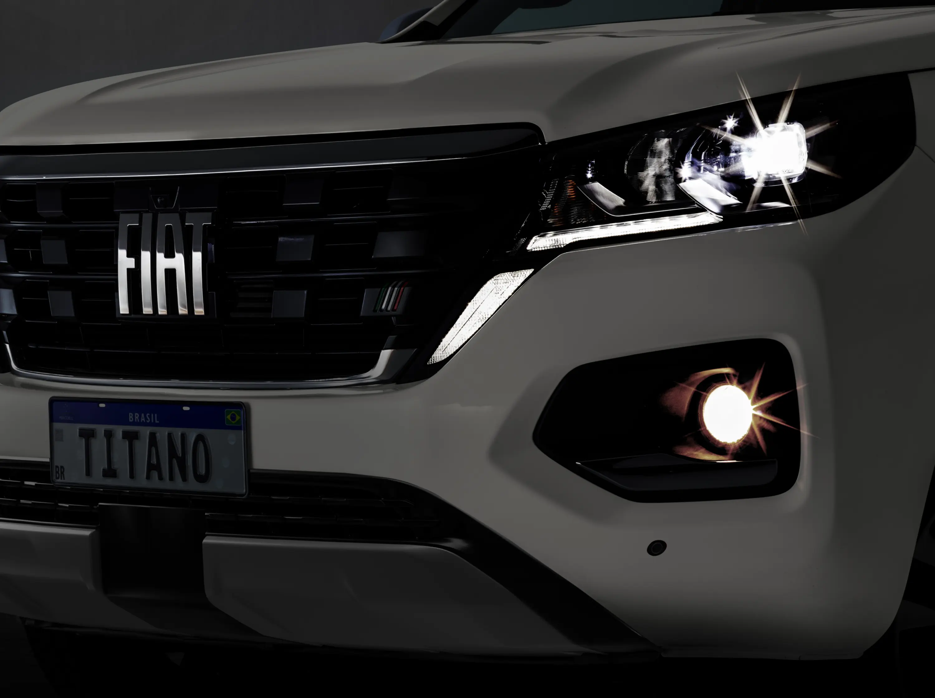 Vista dianteira de Fiat Titano na cor branca, em ambiente escuro com destaque para faróis em LED.